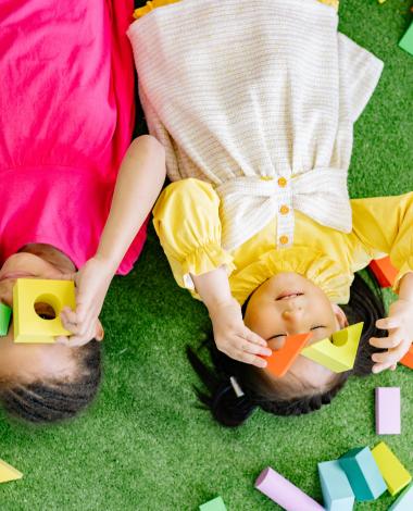 Two kids lying down playing with blocks 