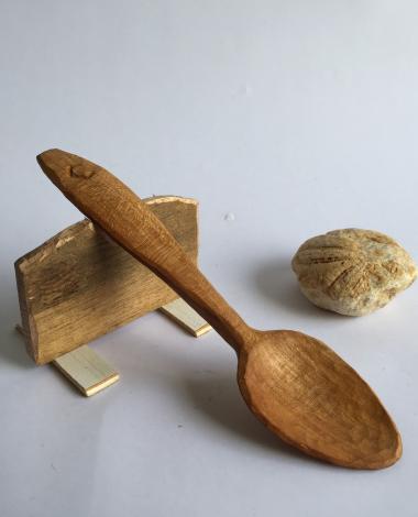 Still life of a hand carved spoon resting on a raised piece of wood. 