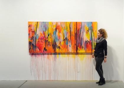 Olga standing next to a multi-coloured painting on a white wall. 