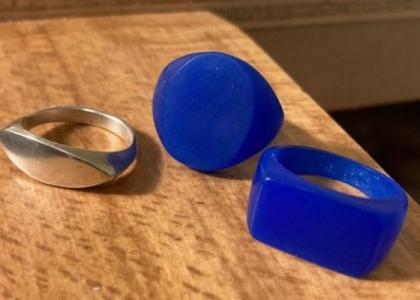 One silver ring and two blue wax casting forms sitting on a table. 