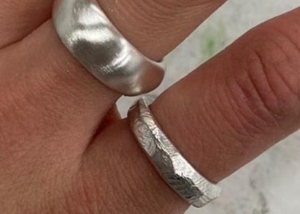 A close up of a hand wearing two silver rings. 