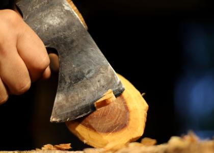 a close up of one student using an axe to carve a spoon. 