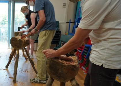 Three student using axes to carve spoons on a wood block. 
