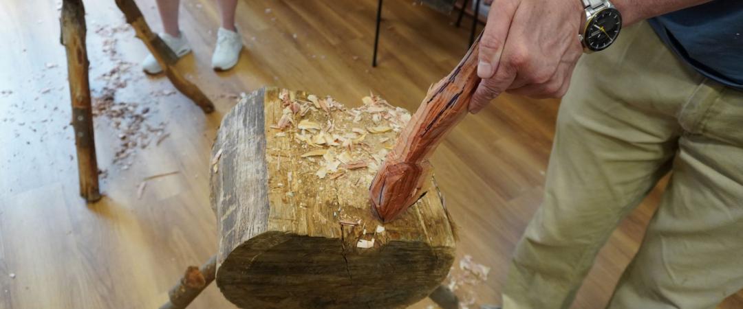 a close up of one student using an axe to carve a spoon. 